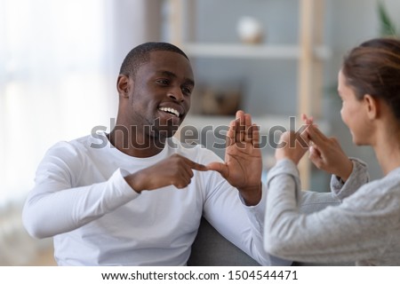Smiling handsome African American man and woman speaking sign language close up, deaf friends or couple communicating, having fun, pleasant conversation, sitting together on couch at home
