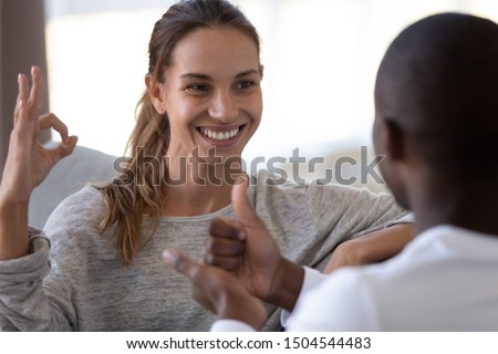 Smiling beautiful woman and African American man speaking sign language close up, deaf friends or couple communicating, having fun, pleasant conversation, sitting together on couch at home Royalty-Free Stock Photo #1504544483