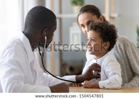 African American male pediatrician with stethoscope listening to lung and heart sound of little boy sitting on mother lap, physician checkup at home or in hospital, children medical insurance care Royalty-Free Stock Photo #1504547801