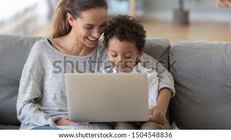 Smiling mother with African American son using laptop close up, happy mum and preschool child sitting on sofa at home, watching cartoons online or play video game, family having fun