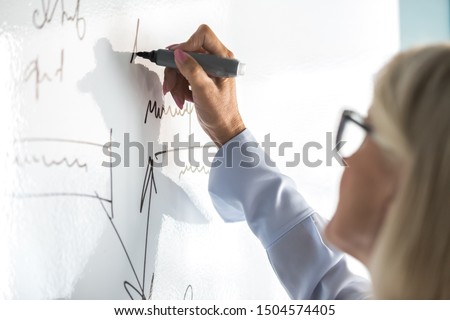 Entrepreneur 50s female writing business plan using flip chart in office close up focus on infographics handwritten information, coach perform presentation on white board concept of training seminar Royalty-Free Stock Photo #1504574405