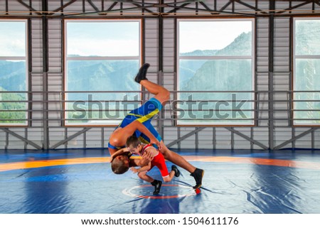 A trainer in sports wrestling tights teaches a little wrestler boy traditional throws in the style of Greco-Roman wrestling against mountains. The concept of children's sports training in martial arts