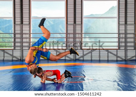 A trainer in sports wrestling tights teaches a little wrestler boy traditional throws in the style of Greco-Roman wrestling against mountains. The concept of children's sports training in martial arts