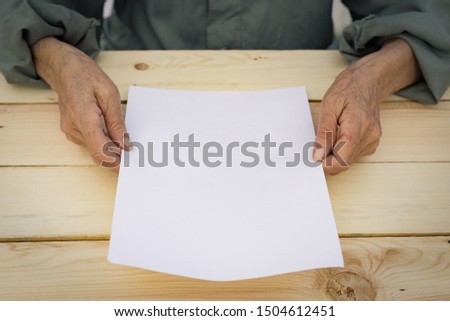 Old hands hold a blank sheet of paper. The concept of new beginnings, active old age, testament. Royalty-Free Stock Photo #1504612451
