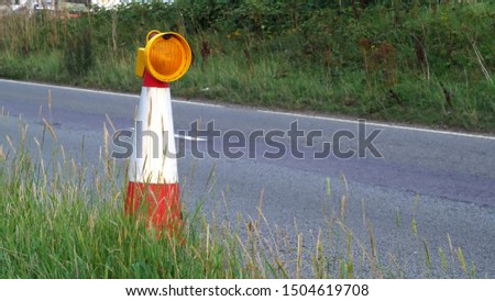 roadworks cone flashing on UK motorway at evening with traffic passing