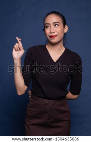 Beautiful young Asian woman cross finger on blue background