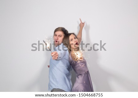 Christmas, new year, party and celebrations concept - young couple with sparklers staying back to back on white background