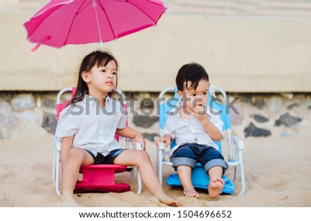 Little girl  and baby boy sitting on a pink beach chair