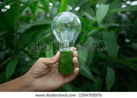 Hand holding light bulb against nature on green leaf with icons energy sources for renewable, sustainable development. Ecology concept