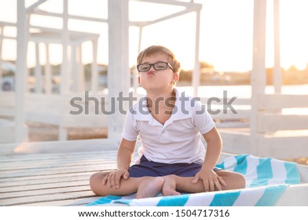Happy boy with down syndrome on a light background of beach loungers . Sea coast. Sunset.