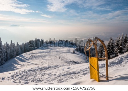 Mountain full of snow with a yellow sledding on the right. Scenic nature winter landscape with hikers in background hiking on snow and having fun. Concept of winter sport like skiing snowboarding. 