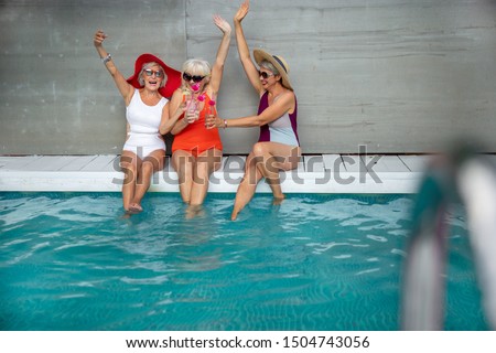 Joyful mature ladies in swimsuits raising hands and toasting with cocktails stock photo