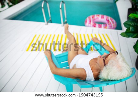 Senior woman in swimsuit sitting in plastic chair stock photo