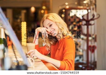 A pretty young lady, sitting at bar, laughs loudly