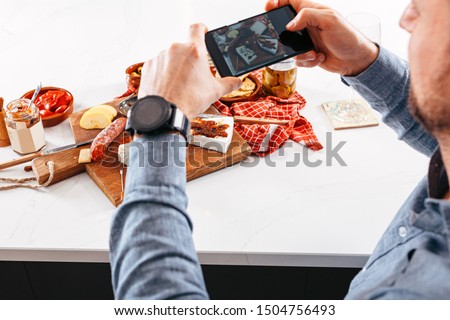 top view with the focus on the background of tapas and appetizers arranged on a white table while a person takes a picture using a mobile phone. foodie, social network, and trend concepts