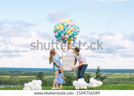 Family mother, father and two daughters beautiful and happy on the green grass with a balloon airship on the background of blue sky with clouds