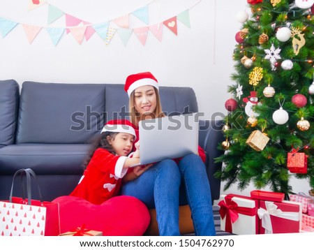 Picture of little girl wearing Santa hat while using a laptop with her mother in Christmas Day