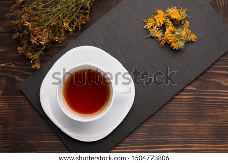 cup of herbal tea on slate board on a wood table. 
calendula and 
St. John's wort grass 