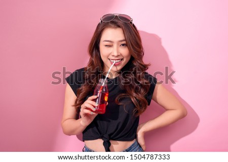 portrait of beautiful happy cute woman girl in casual  summer clothes drink red soda water from bottle with straw over pink background