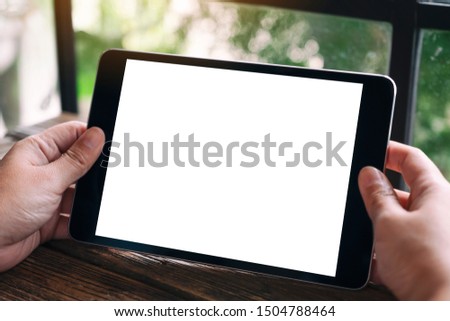 Mockup image of hands holding black tablet pc with blank white desktop screen 