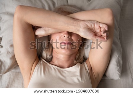 Sleepless mature woman suffering from insomnia close up, lying in bed, older female covering eyes with hands, trying to sleep, nightmares or depression, feeling headache or migraine Royalty-Free Stock Photo #1504807880