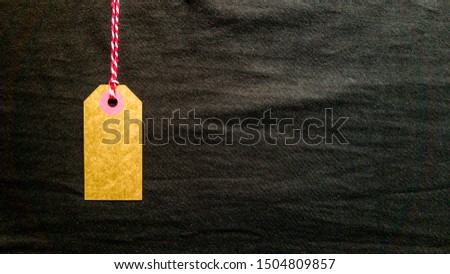 Brown cardboard tag hanging on a red rope on a black background from fabric. Copy space, place for text, flat lay.