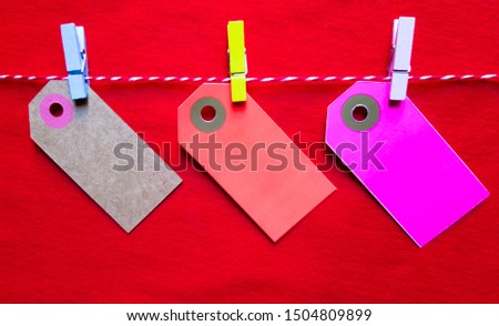 Colorful paper notes and clothespins on a red background. Empty color cardboard price tags, sale tag, gift tag, address label, luggage label hanging on clothes. Wooden clips. Layout, copy space for