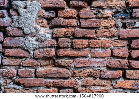The cement wall is broken up to see a brick wall.