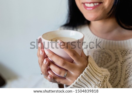 Close up of a beautiful young woman hands holding a cup of hot coffee in winter outfit at home