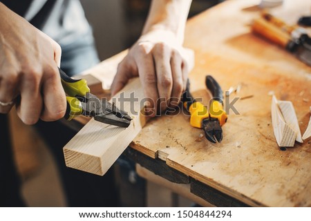 A man carves a tree. The carpenter works with pliers in a studio. An engineer provides a tree shape Royalty-Free Stock Photo #1504844294