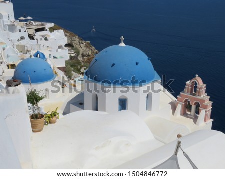 The beautiful blue domes on the whitewashed cubiform architecture in  the Greek Village of Oia, on the Island of Santorini in the Aegean Sea are pictured along side lovely bell structures. Royalty-Free Stock Photo #1504846772