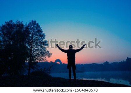 Photo from back of man with hands up at sunset