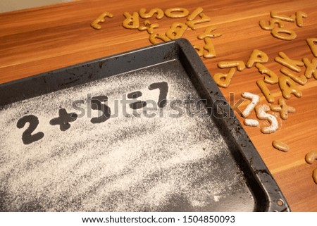 on a baking tray sprinkled with icing sugar or flour, the equation 2+5=7 is written