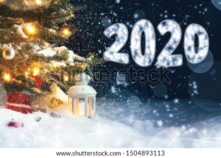 Christmas card - gifts and a lantern in the snow under a Christmas tree decorated with lights and Christmas decorations, and inscription 2020
