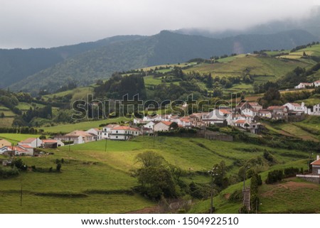 Fresh green nature with fields, meadows. pastures and a small village. Cloudy rainy sky. Sao Miguel, Azores Islands, Portugal.