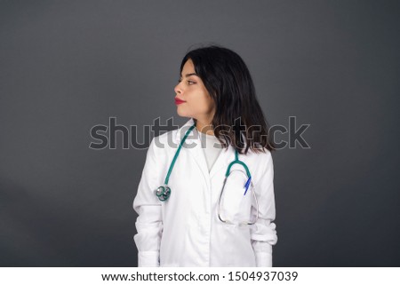 Profile of doctor woman with healthy pure skin has braided hairstyle wears black clothes has contemplative expression ready to have outdoor walk isolated over grey studio wall with copy space.