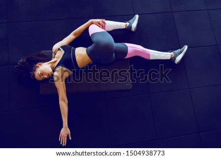 Top view of muscular brunette in sportswear lying on the mat in gym and doing stretching exercise.