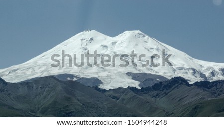Amazing perspective of caucasian snow mountain or volcano Elbrus with green fields, blue sky background. Elbrus landscape view - the highest peak of Russia and Europe.