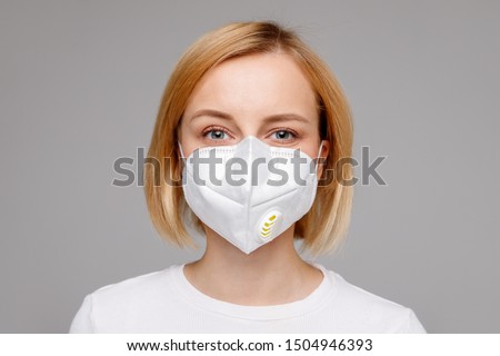 Studio portrait of young woman wearing a face mask, looking at camera, close up, isolated on gray background. Flu epidemic, dust allergy,  protection against virus. City air pollution concept  Royalty-Free Stock Photo #1504946393