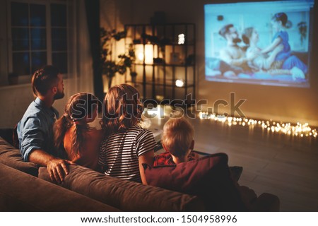 family mother father and children watching projector, TV, movies with popcorn in the evening   at home  Royalty-Free Stock Photo #1504958996