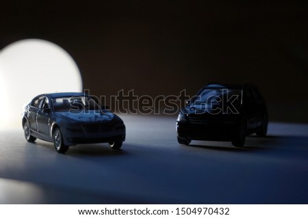 Silhouettes of two scale models of a sedan car and a SUV 4×4 all terrain vehicle in the dark, with white light, shadows and clair-obscur effects