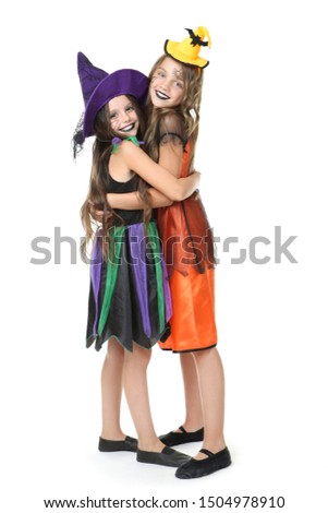 Two young girls in halloween costumes hugging each other on white background