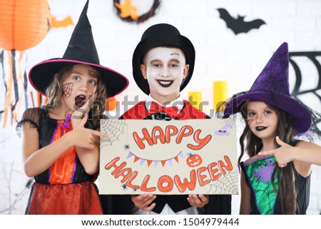 Young two girls and boy in costumes holding paper with text Happy Halloween