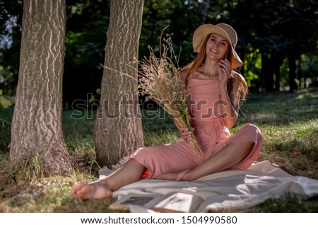 Beautiful girl resting on the grass by the tree. In a hat with a book of dried flowers and a smartphone.