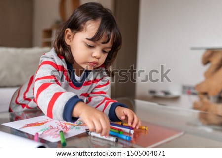 Adorable little girl sitting at a table in her living room at home drawing pictures with crayons