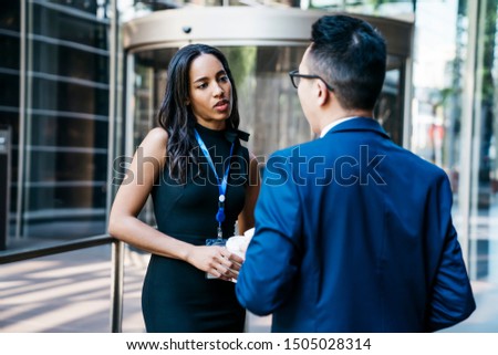 Beautiful African American woman in black dress and name tag talking to male colleague being on conference and standing on street