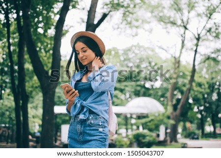 Beautiful woman typing text message for send via cellphone application enjoying free time for spending day in city park, trendy dressed Ukrainian female blogger searching information on website