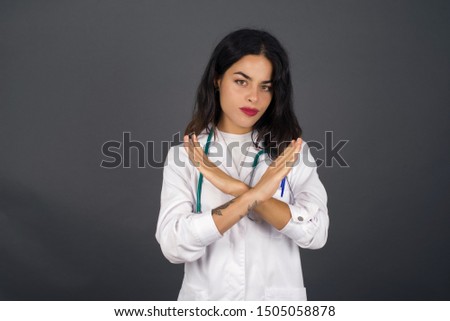 Young beautiful doctor girl wearing medical uniform standing over isolated background. Has rejection angry expression crossing hands doing refusal negative sign.