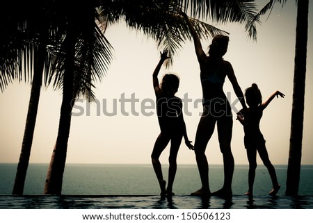 silhouette of a woman and two young girls standing by the pool on sea background