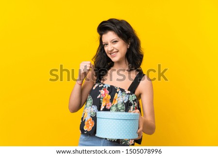 Young woman over isolated yellow background holding gift box